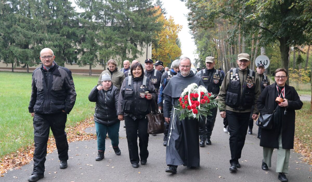 Uczestnicy uroczystości z wiązanką kwiatów idą alejką na cmentarz zakonny w Niepokalanowie