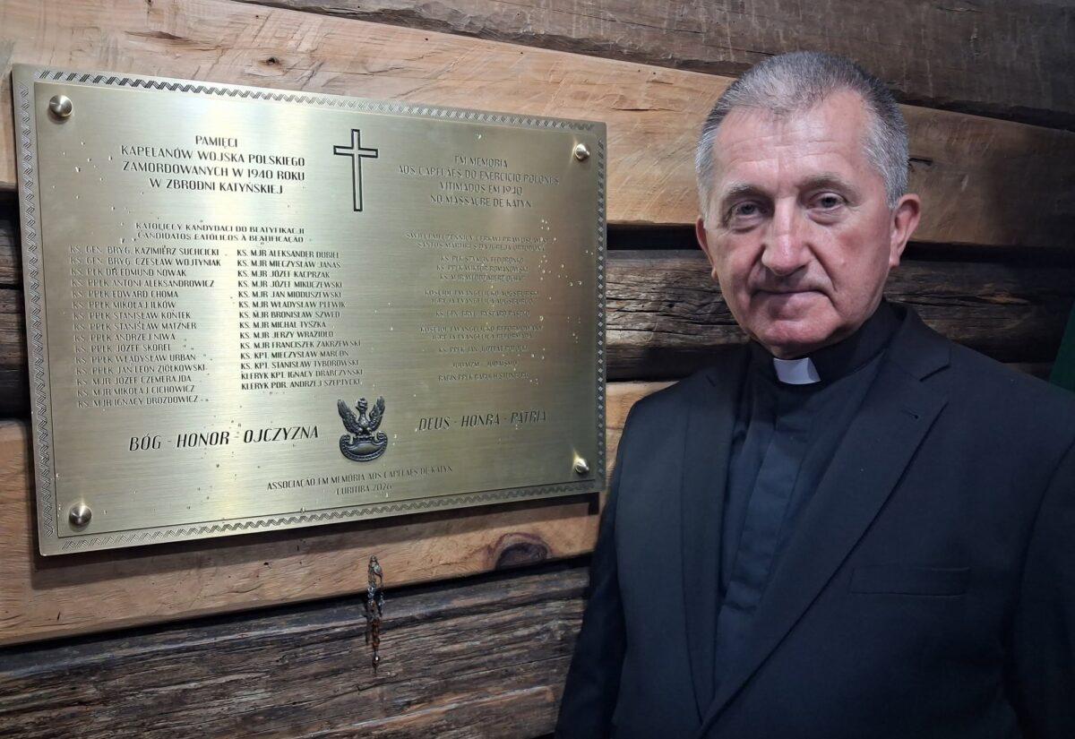 Tablica upamiętniająca Kapelanów Katyńskich na drewnianej ścianie kaplicy Matki Bożej Częstochowskiej w Parku św. Jana Pawła II w Kurytybie; obok kapłan w stroju duchownym