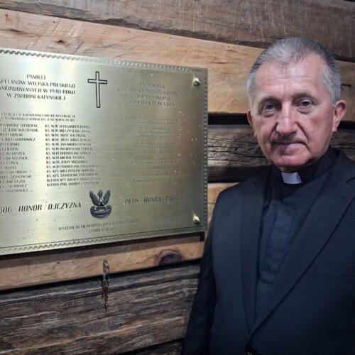 Tablica upamiętniająca Kapelanów Katyńskich na drewnianej ścianie kaplicy Matki Bożej Częstochowskiej w Parku św. Jana Pawła II w Kurytybie; obok kapłan w stroju duchownym